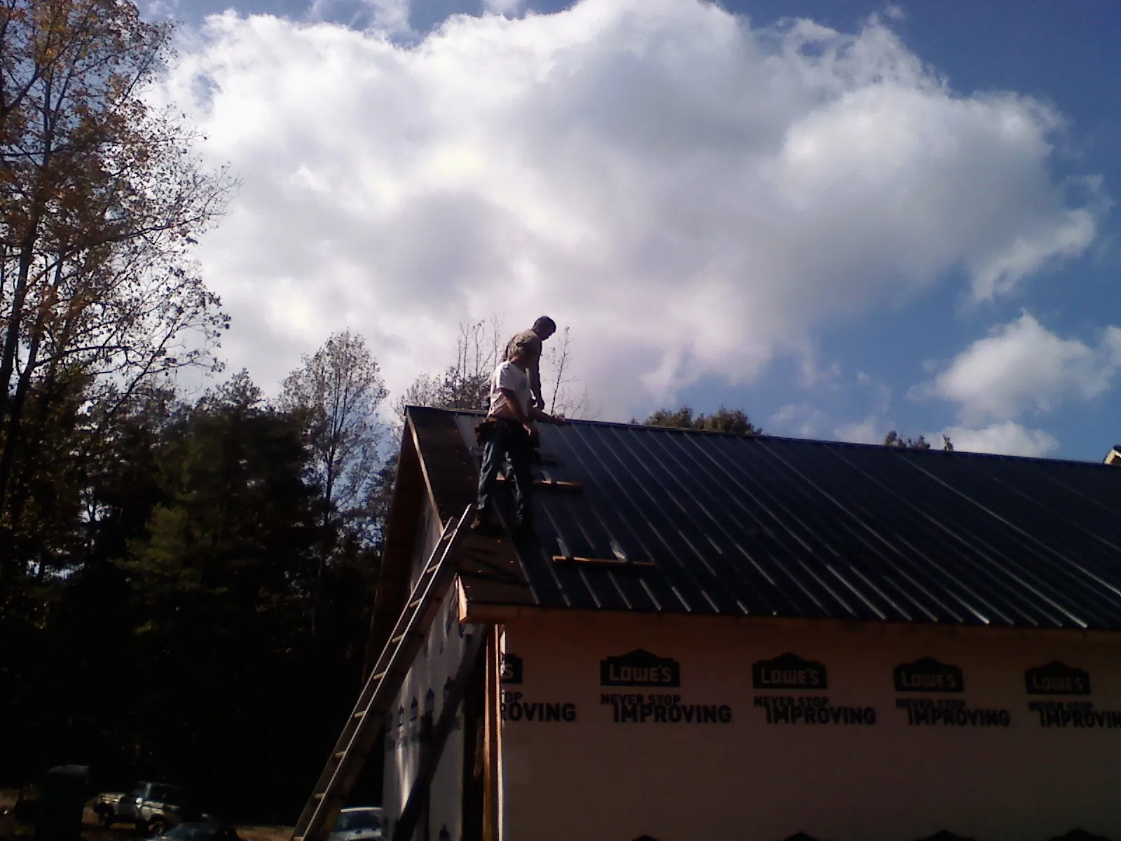 Roofer fastening dark metal panels high against a cloudy sky, from a Roof Inspection job in Hamilton